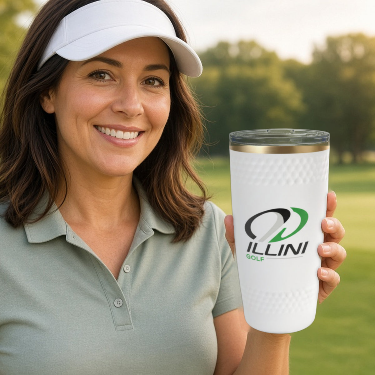 Woman on a golf course holding a white 20oz dimpled golf ball tumbler printed with a custom Illini Golf logo